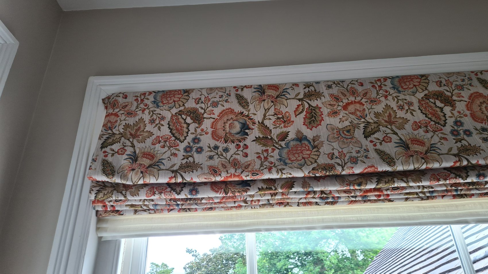 A traditional floral print made up as a deep Roman blind for a bay. On a wide window the fold depth has to be worked out from the drop, or the blind ends up looking either starved or top-heavy when it is raised.