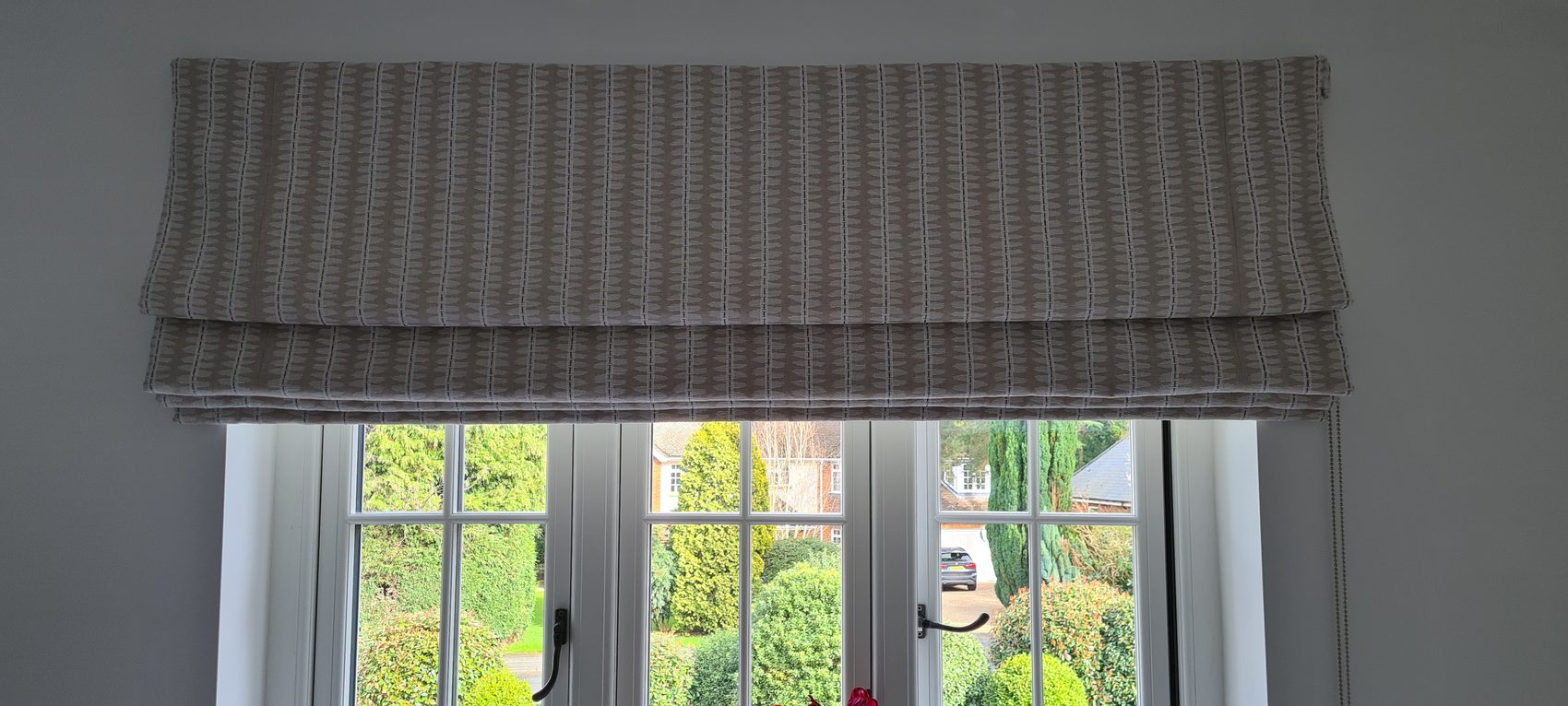 A textured stripe made up as a Roman blind over French doors, fitted outside the reveal so the folds sit clear of the glass when the blind is up and nothing blocks the handles.